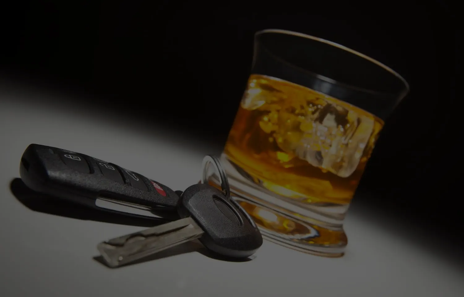 Car keys resting on a table beside a glass of whisky on ice
